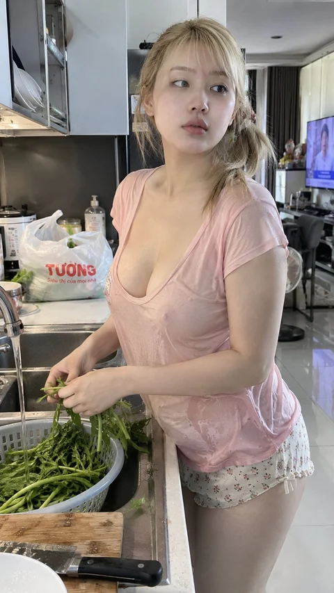 A person in a pink shirt prepares green vegetables at a kitchen counter.